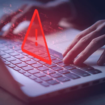 A person's hands typing on a laptop, overlaid with a red caution symbol, indicating a cybersecurity alert or warning.