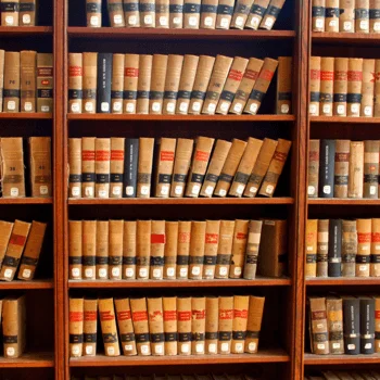 Rows of aged books neatly arranged on wooden shelves, featuring red and black spines with labels, in a historic library setting.