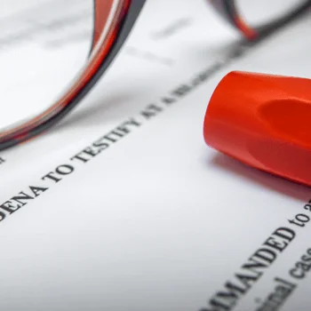 Close-up of glasses and a red highlighter resting on a legal document titled "Subpoena to Testify," indicating legal proceedings.