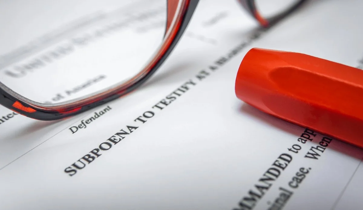 Close-up of glasses and a red highlighter resting on a legal document titled "Subpoena to Testify," indicating legal proceedings.