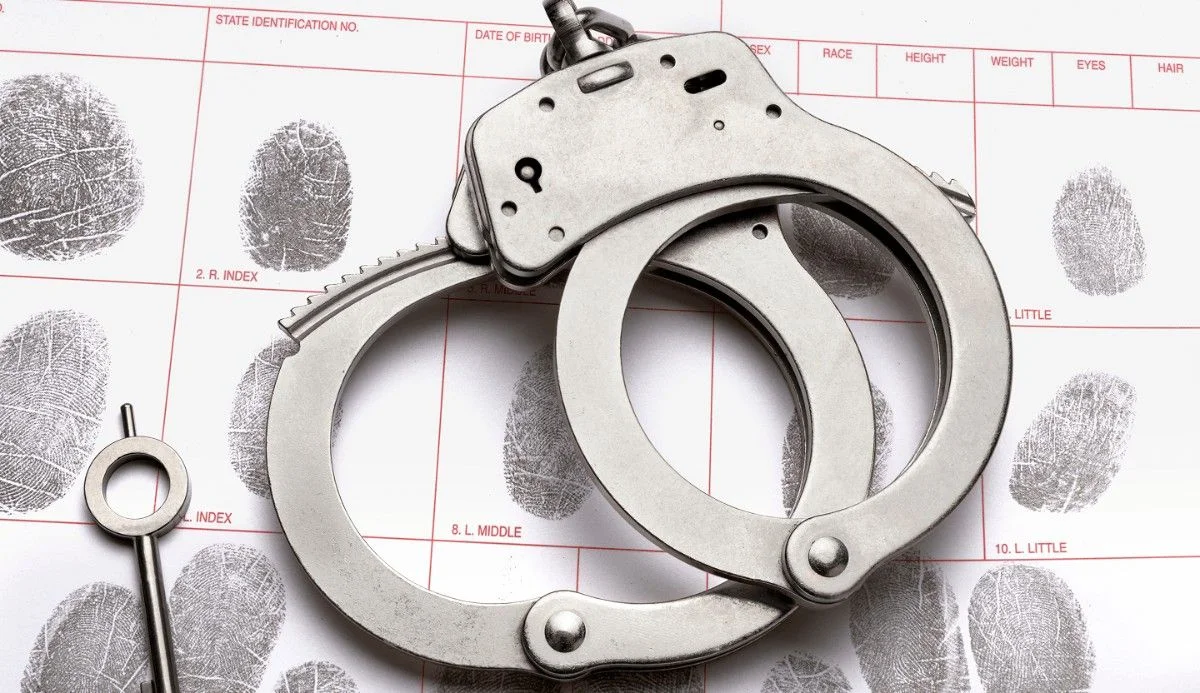 A pair of silver handcuffs rests on a fingerprint identification form, highlighting crime scene and forensic elements.