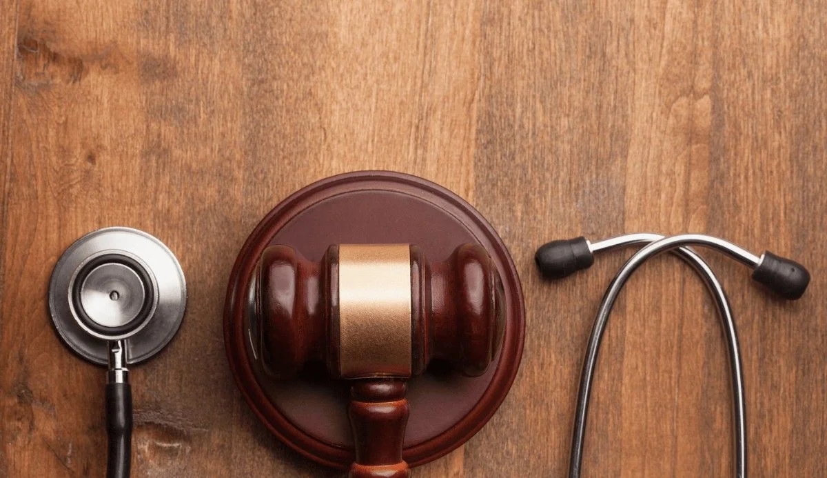 A wooden gavel and a stethoscope lie side by side on a rustic wooden surface, symbolizing the intersection of law and medicine.