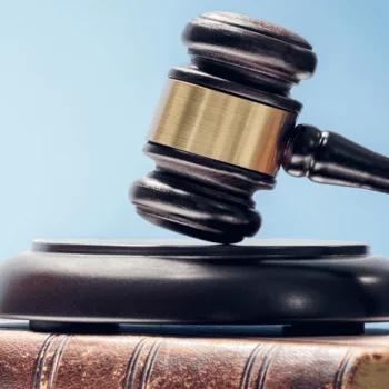 A gavel rests on a wooden block, placed atop a closed book, with a light blue background, symbolizing justice and law.