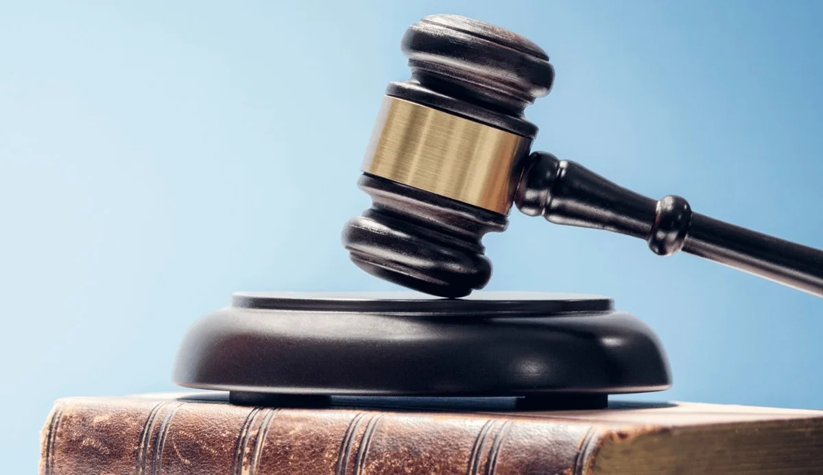 A gavel rests on a wooden block, placed atop a closed book, with a light blue background, symbolizing justice and law.