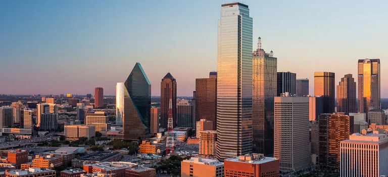 Panoramic view of Dallas skyline at sunset, showcasing modern skyscrapers and urban landscape bathed in warm golden light.