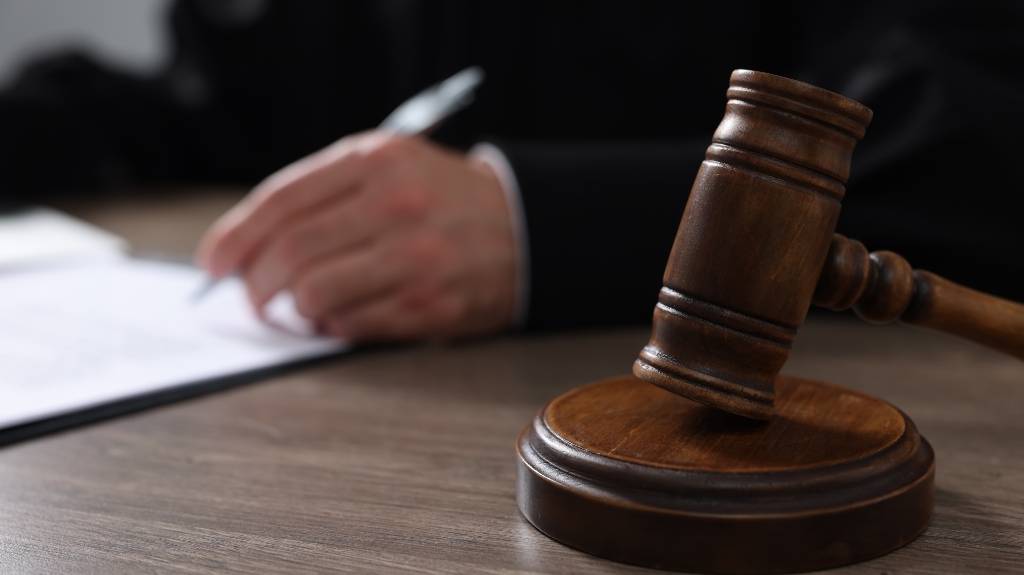 Judge with gavel writing in papers at wooden table