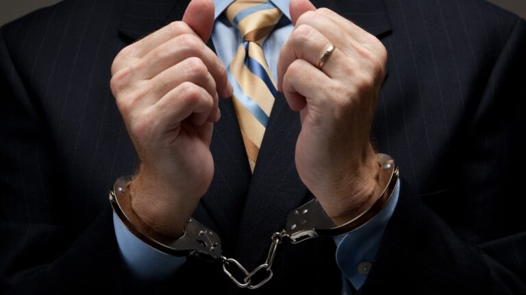 A man in a blue business suit holding hands in handcuffs