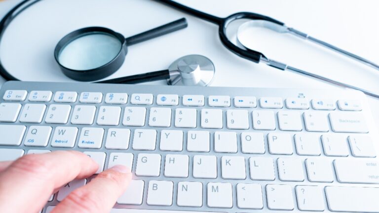 Medical stethoscope and magnifying glass on laptop keyboard