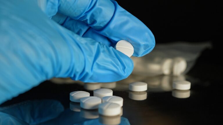 man's hand in blue gloves examines pills